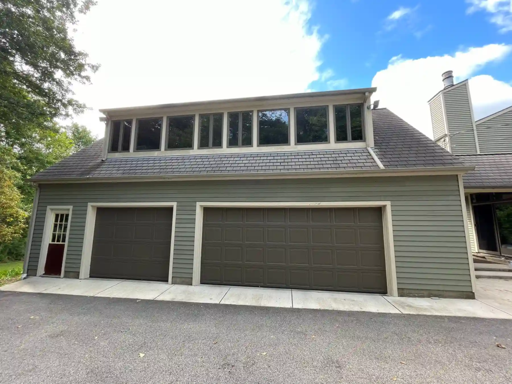 A Light Olive Green Painted Garage with Cream Accents and Two Brown Garage Doors Shines in the Spring Sun.