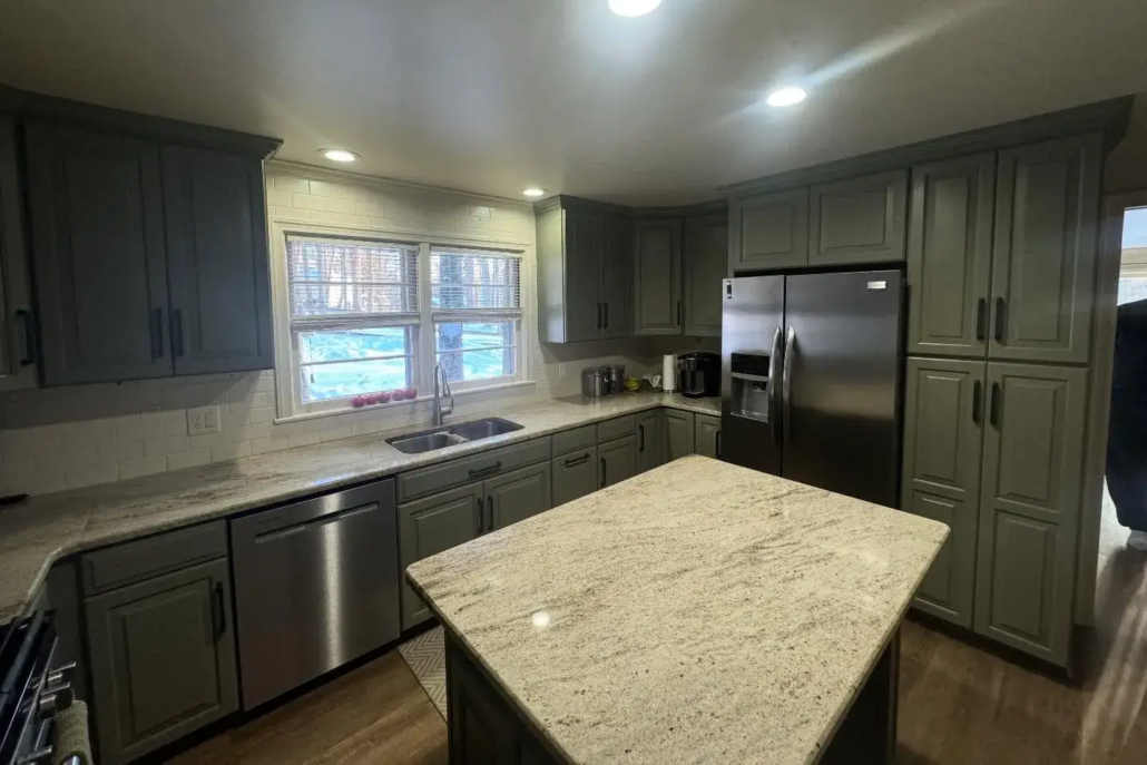 Dark, Olive Green Painted Kitchen Cabinets Reflect off of the Canfield Home's White Countertops.