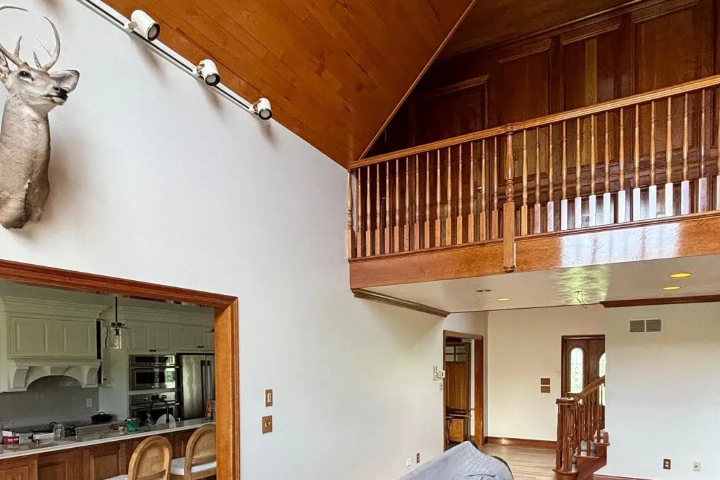 Bright Light Fills a White Painted Living Room with High Ceilings and a Second Floor Wooden Banister.